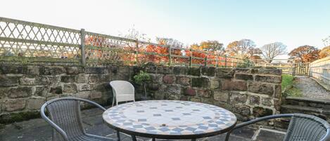 A round outdoor table with a mosaic tile top, surrounded by wicker chairs.