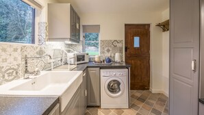 A compact kitchen with a built-in washing machine, a microwave, and a sink. - Woodpeckers Cottage (Church Stretton)