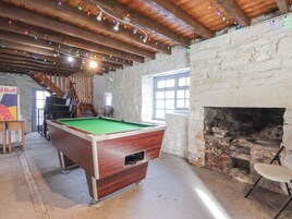 A billiards table in a rustic room with a stone wall and wooden beams.