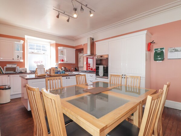 Una cocina moderna con armarios blancos, una isla central y una zona de comedor con una mesa de vidrio y sillas de madera.