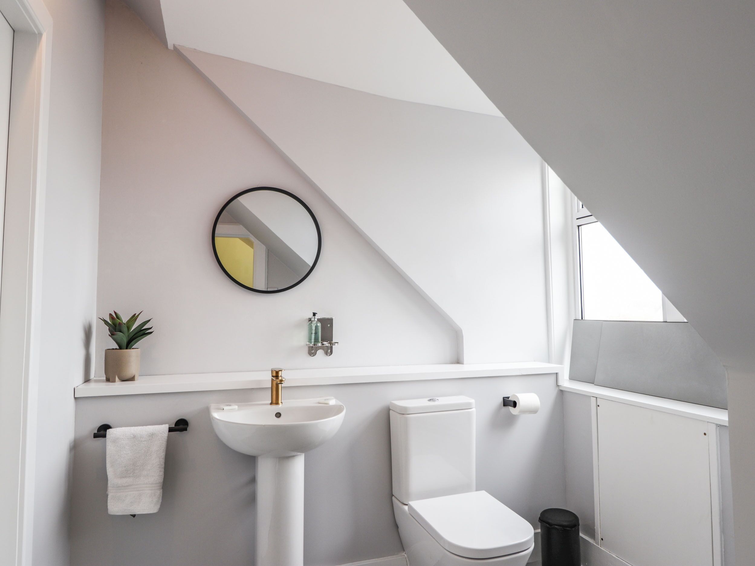 A modern bathroom with a white sink, toilet, and a small potted plant.