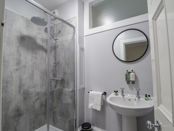Une salle de bain avec une douche à parois de verre, un lavabo blanc avec un miroir au-dessus, et une serviette suspendue à un porte-serviettes.