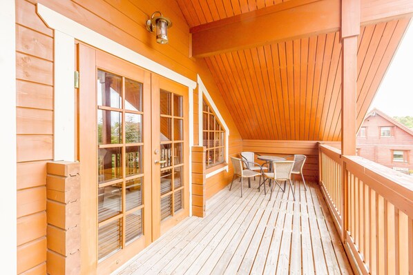 A wooden deck with a table and chairs, a covered area with a sloped ceiling, and large windows with glass doors. - Jamaal Lodge (Morpeth)