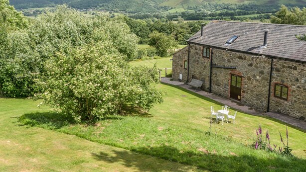 A stone building with a sloped roof, a grassy yard, and a view of rolling hills in the background. - Hope Hall Barn (Shrewsbury)