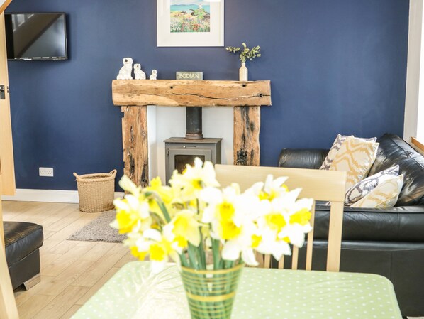A living room with a fireplace, a sofa, and a table with flowers. - Bodfan Peniel (Llanerchymedd)