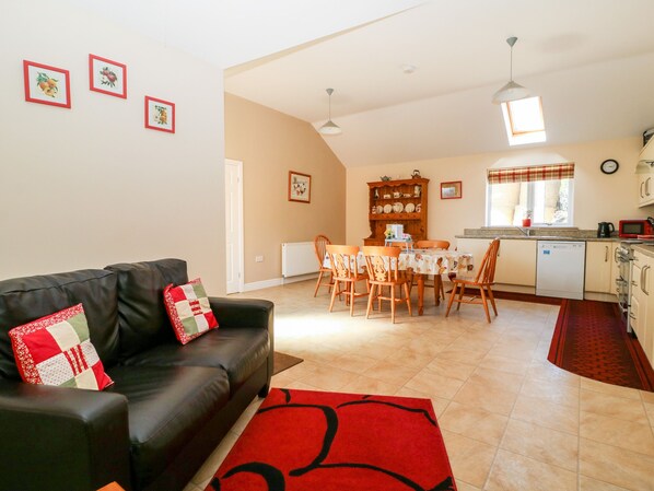 A living room with a black leather sofa, a red rug, and a dining area with a table and chairs. - 2 Pines Farm Cottages (Tadcaster)