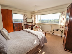 A bedroom with a large bed, a desk, a chair, and a wardrobe.
