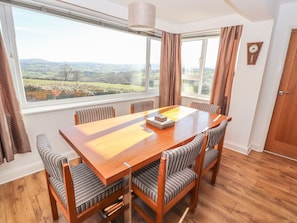 A dining room with a wooden table and striped chairs, large windows with curtains, and a view of the countryside.