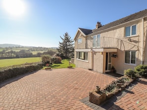 A two-story house with a brick patio, a stone wall, and a view of rolling hills.