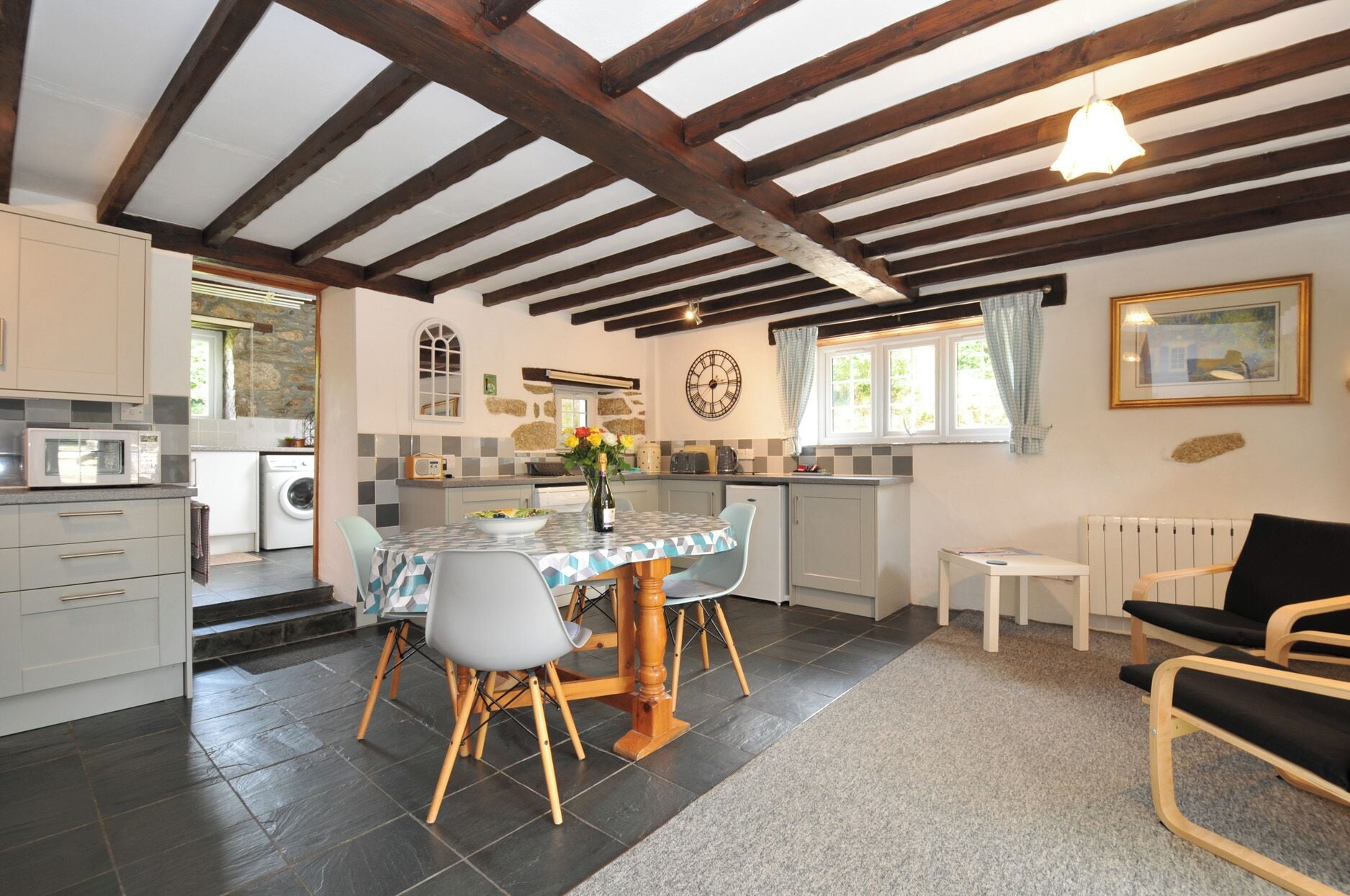 Une cuisine avec une table à manger, des chaises et une horloge au mur.