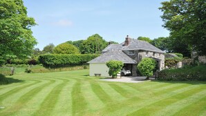 A stone house with a garage, surrounded by a well-maintained lawn and trees. - Trevenning Barn (Bodmin)