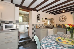 A compact kitchen with a microwave, washing machine, and a clock on the wall.