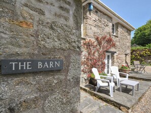 A stone building with a sign reading 'THE BARN' and outdoor seating with white chairs and tables.