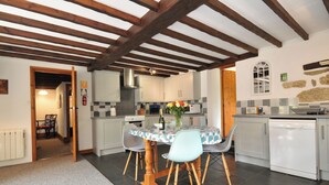 A kitchen with a dining table, chairs, a stove, and a dishwasher. - Trevenning Barn (Bodmin)