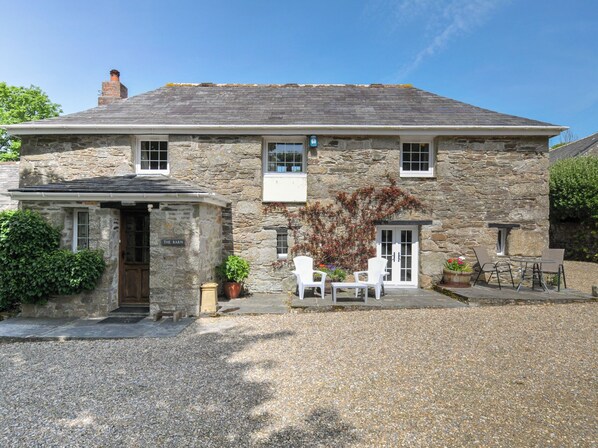 A stone building with a gravel driveway, a small porch with white chairs, and a sign reading 'The Barn.'