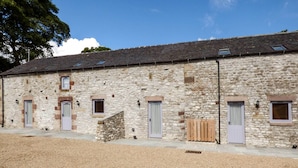 A stone building with multiple doors and windows, a gravel driveway, and a stone wall. - Corner Croft (Buxton)