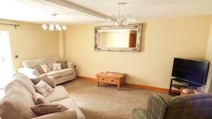 A living room with a beige sofa, a plaid sofa, a small wooden table, a television, and a mirror on the wall. - Corner Croft (Buxton)