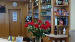 Una zona de bar con mostrador, un jarrón de rosas rojas y estanterías llenas de botellas y copas.