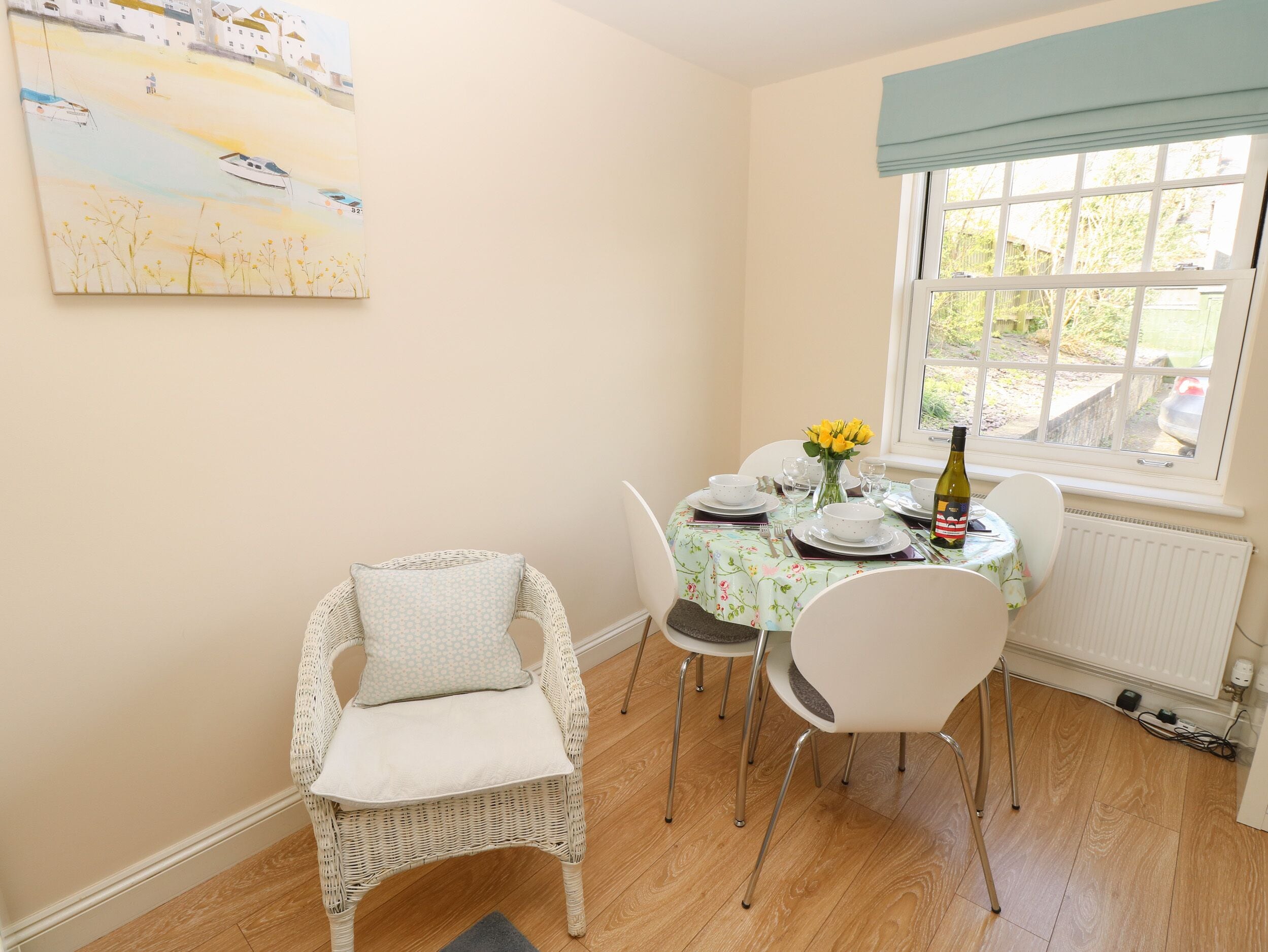 Comedor con una mesa dispuesta para cuatro, una silla de mimbre y una ventana con vistas a zonas verdes.