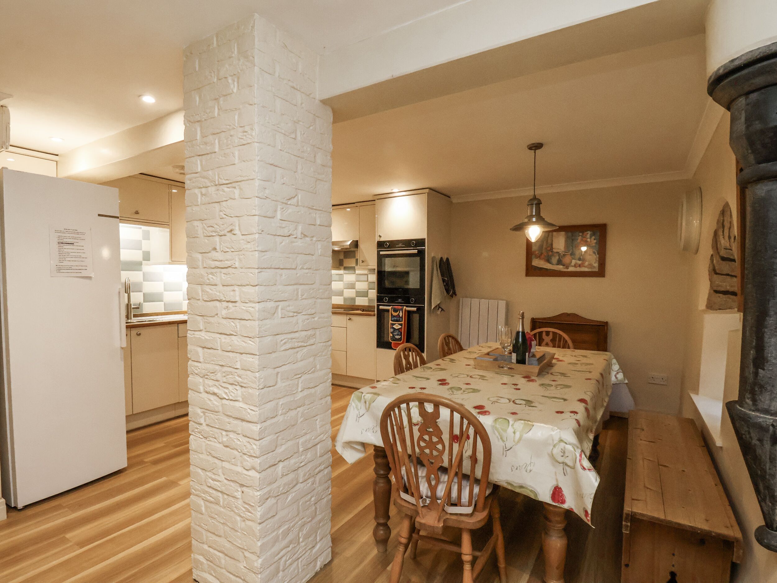 A dining area with a table set for four, surrounded by wooden chairs. A white brick pillar stands in the middle.