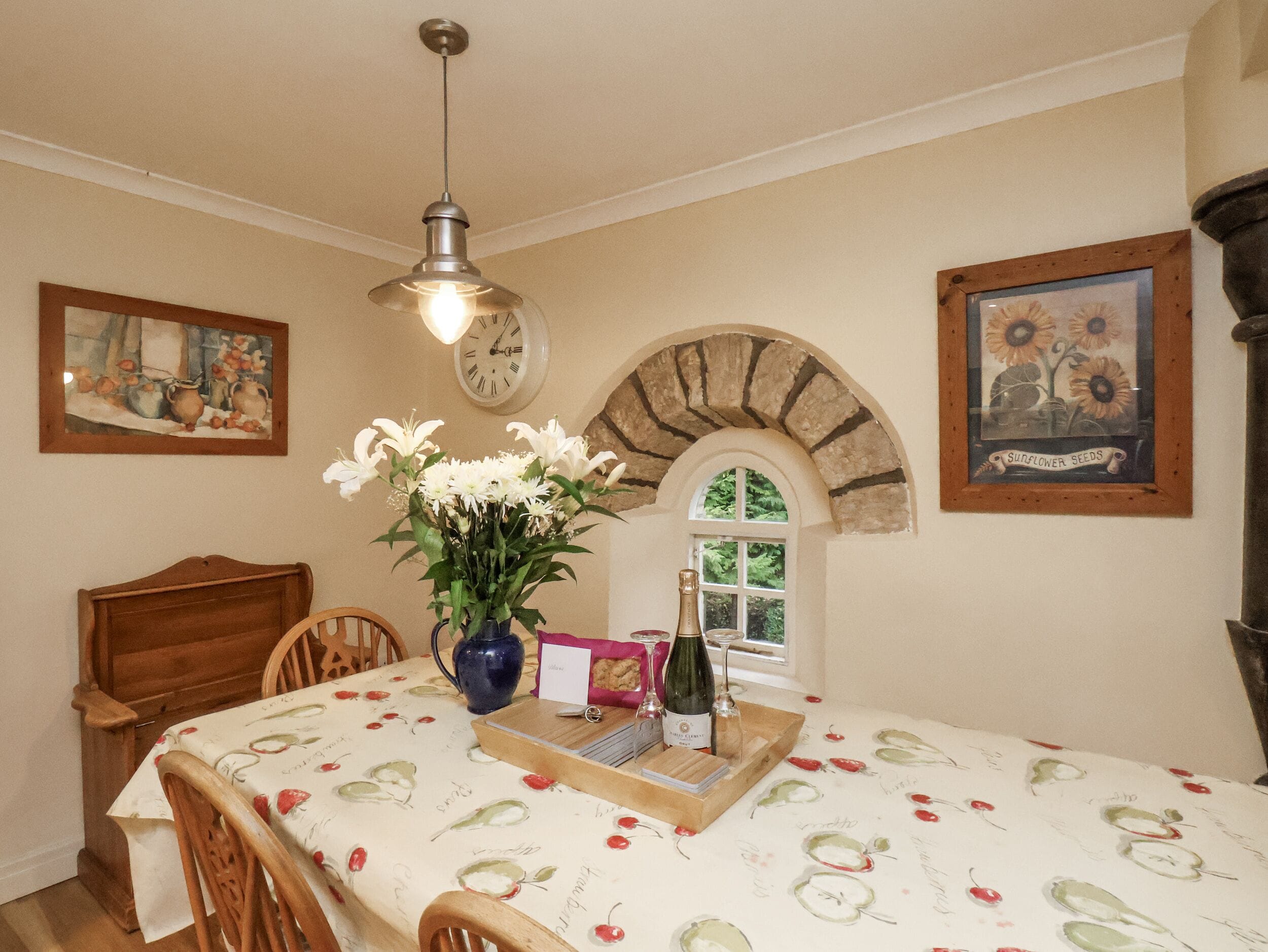 A dining area with a table set for two, a vase of flowers, a bottle of wine, and a tray with glasses and a menu.