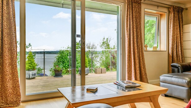 En moderne stue med en stor skydedør, der fører ud til en balkon med udsigt over et søområde.