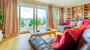 En moderne stue med sofa, sofabord og en skydedør til en balkon med plantekasser.