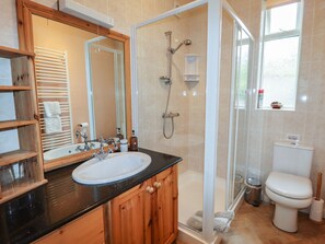 Un baño con tocador de madera, lavamanos, espejo, ducha e inodoro.