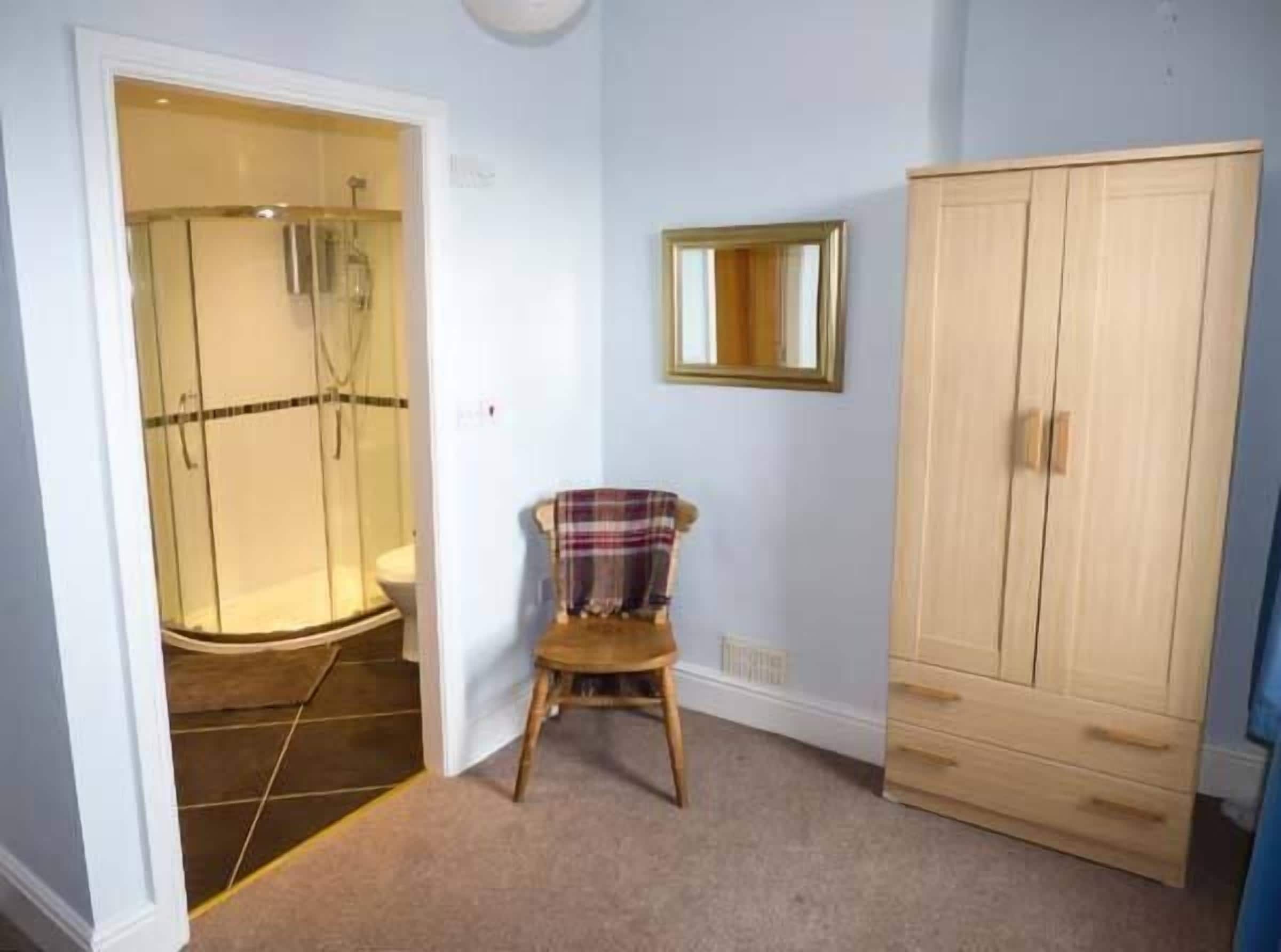 Een badkamer met een douche, een houten stoel en een kledingkast.