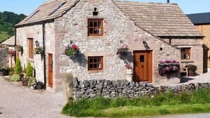 A stone cottage with a sloped roof, wooden door, and windows. - The Cow Barn (Bakewell)
