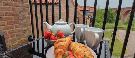 A breakfast setup on a balcony with croissants, strawberries, a teapot, and two cups.