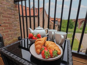 Un plateau de petit-déjeuner installé sur un balcon, avec des croissants, des fraises, une théière et deux tasses.