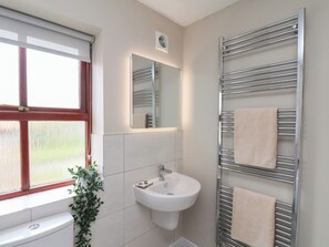 Une salle de bain moderne avec un lavabo blanc, un miroir, un porte-serviettes et une fenêtre donnant sur un paysage verdoyant.