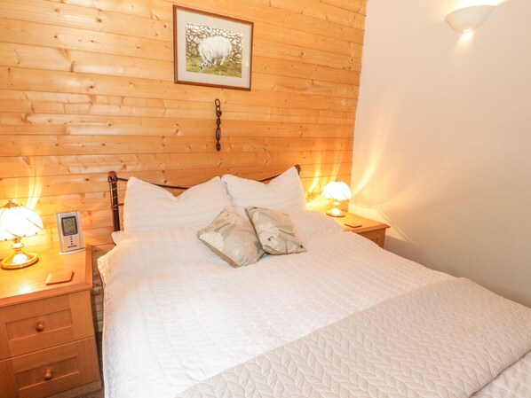 Una cama bien hecha con ropa blanca, dos lámparas de noche, un termostato y un cuadro en la pared de madera.