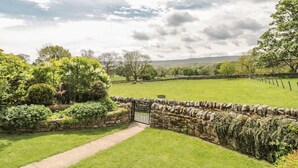 A private garden with a stone wall, a paved path, and a view of a green field and trees. - Hoodgill Barn (Barnard Castle)