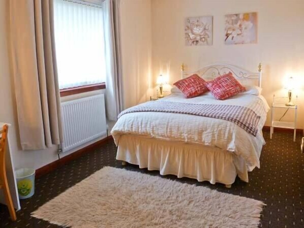 A bedroom with a bed, two bedside lamps, a radiator, and a window with curtains. - Ardmore (Waternish)