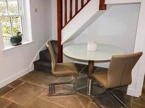 A corner room with a round glass table, two beige chairs, a small white table lamp, and a stone vase on the windowsill. - 1 Primitive Croft (Buxton)