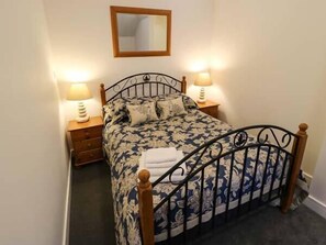 A neatly made bed with a floral bedspread, two bedside lamps, a wooden nightstand, and a mirror on the wall. - 1 Primitive Croft (Buxton)