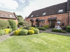 A brick building with a garden area, a paved walkway, and a small outdoor seating area with tables and chairs.