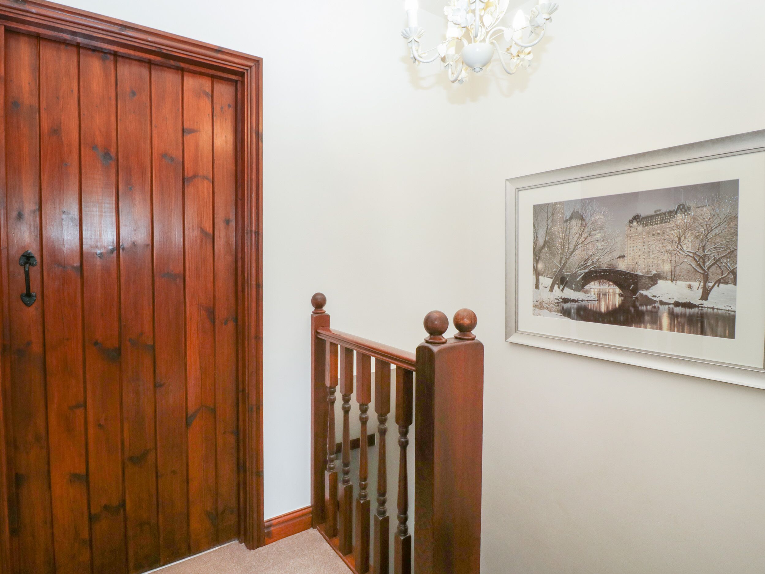 A wooden door, a staircase with a balustrade, and a framed picture on the wall.