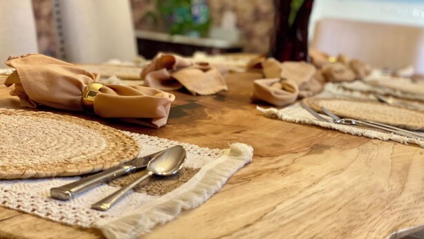 A wooden table with a placemat, a spoon, a knife, and a folded napkin.
