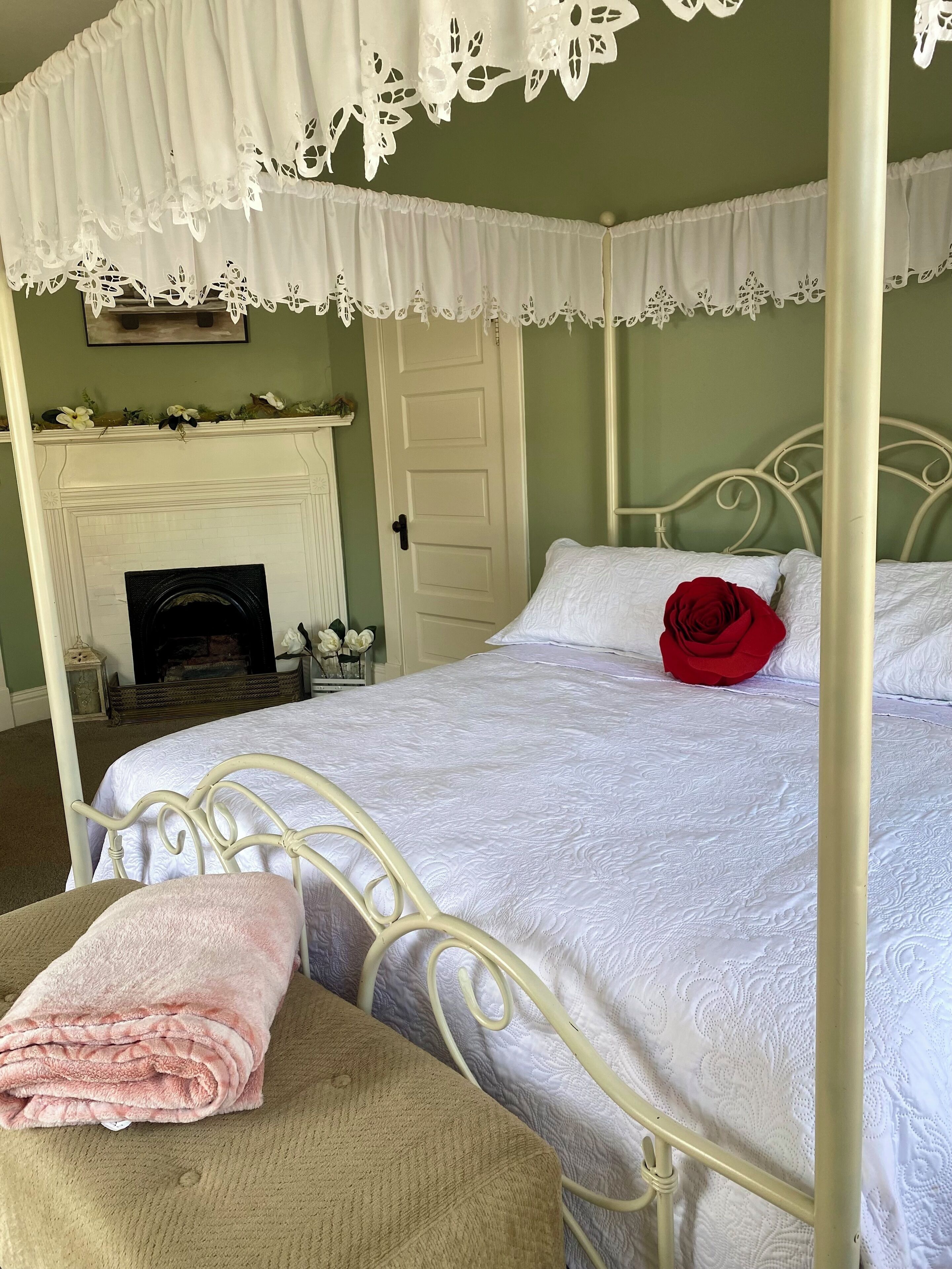 A four-poster bed with a white bedspread and a red rose decoration.