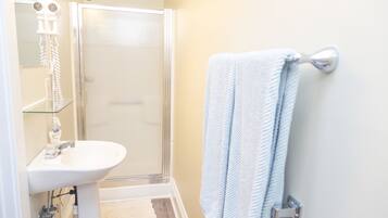 Un baño con cabina de ducha de vidrio, un lavabo blanco y una toalla colgada en un tendedero de metal.