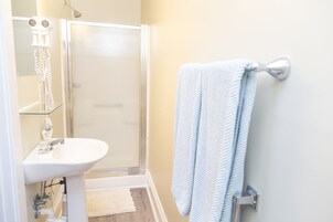 Un baño con cabina de ducha de vidrio, un lavabo blanco y una toalla colgada en un tendedero de metal.