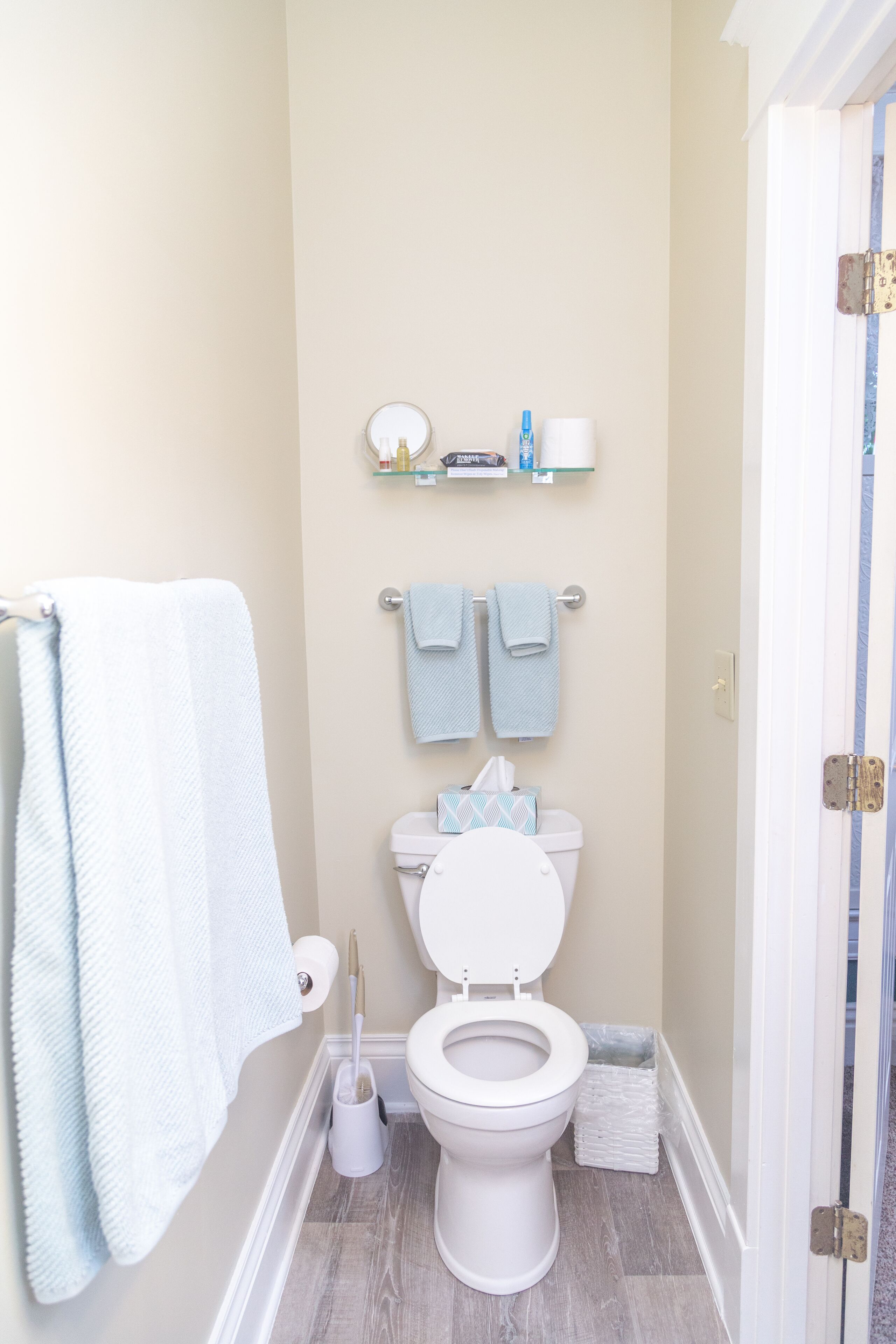 Un bagno con il water, un lavandino e uno specchio. Asciugamani appesi al muro e uno scaffale con articoli da toilette.