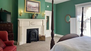 A bedroom with green walls, a white fireplace, a bed, a red armchair, and a ceiling fan.
