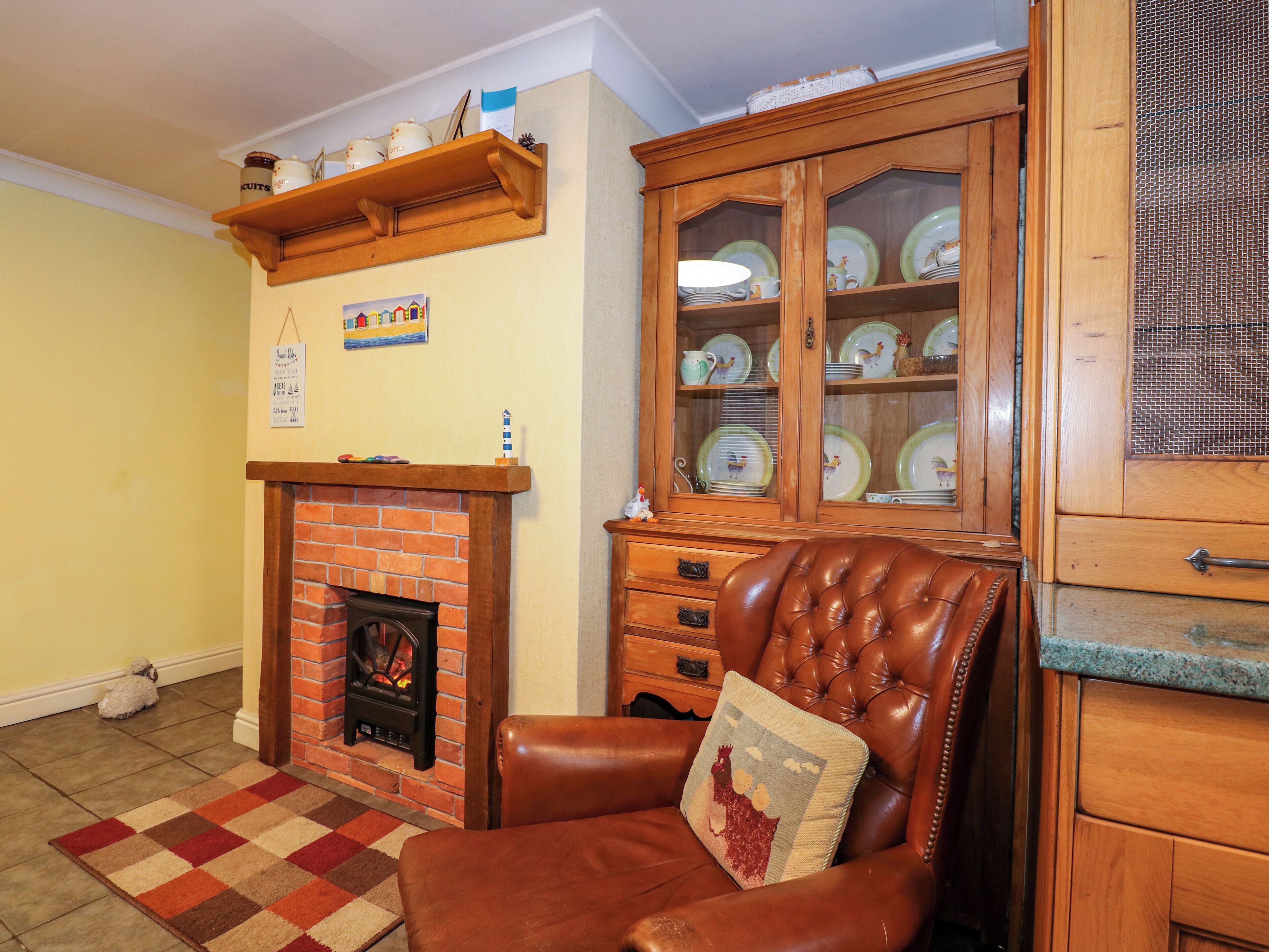 A cozy living room with a brick fireplace, a leather armchair, and a china cabinet.