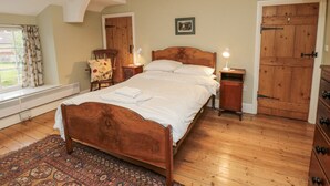 A bedroom with a wooden bed, a chair, a nightstand, a dresser, and a window with curtains. - Brookleigh (York)