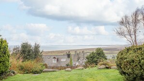 A grassy area with a stone building and a castle in the background. - The Villa (Harlech)