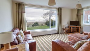 A living room with leather sofas, a television, and a view of a green landscape through large windows. - The Villa (Harlech)
